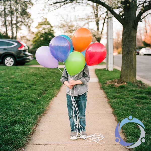A little boy holds balloons in front of his neighborhood as a representation of giving back to the community.