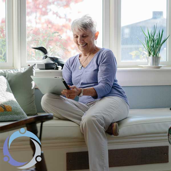 As an older woman sits with an iPad, she is learning how to delegate caregiving tasks using Lotsa Helping Hands.