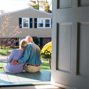 An older couple sits outside their house while discussing their options for in home care. 