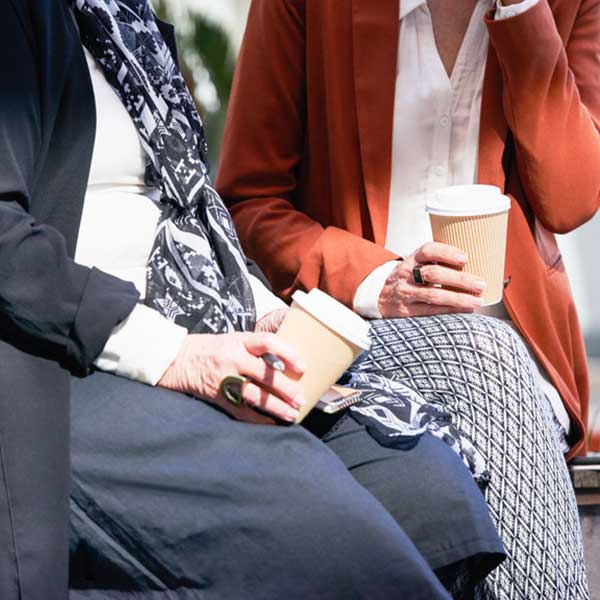 As two women talk over coffee, spending time with friends is one of the recommended ways to save your sanity while caregiving.